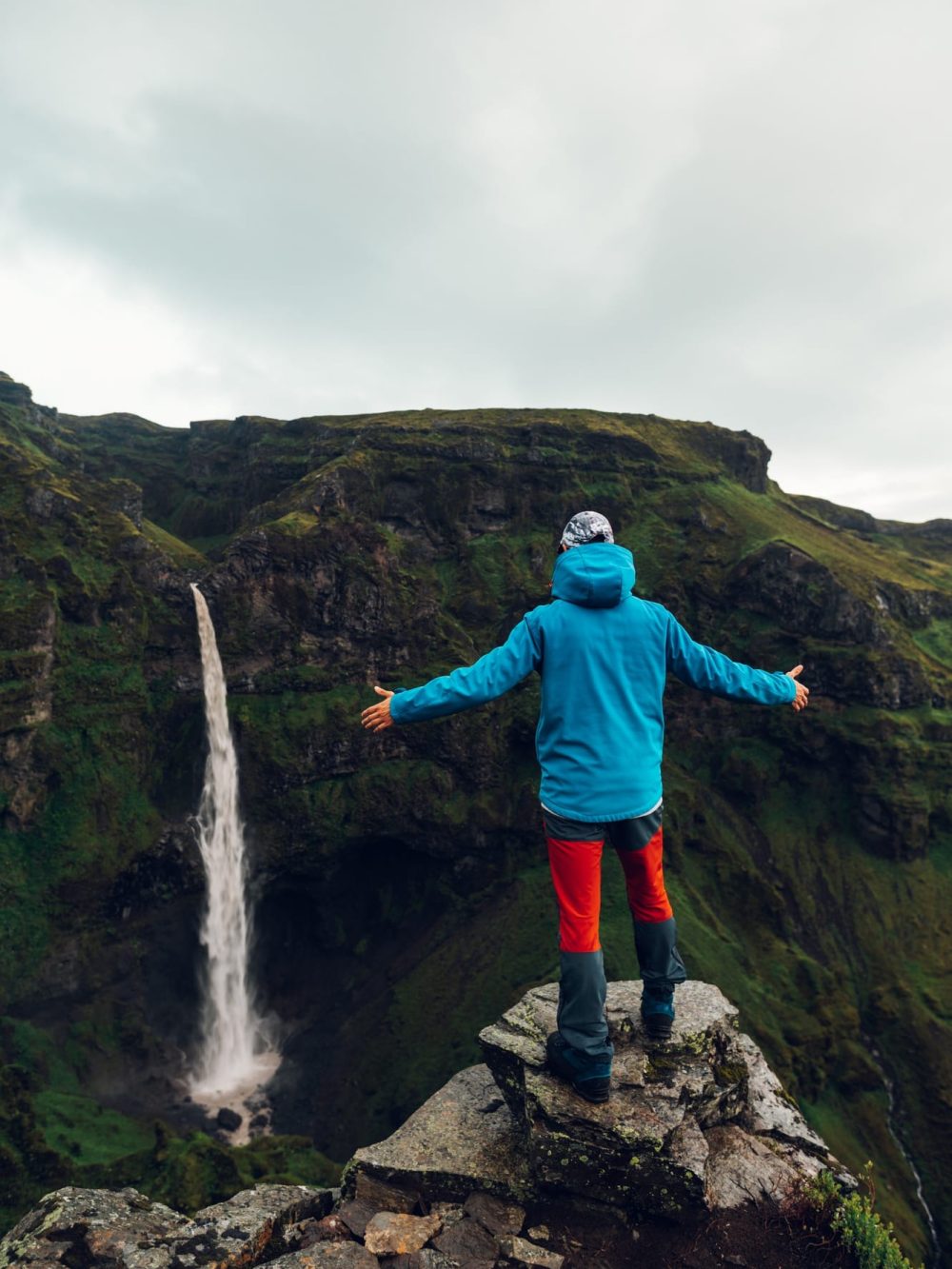 An adventurer on a cliff is watching down on the waterfall while standing in the nature of Iceland.